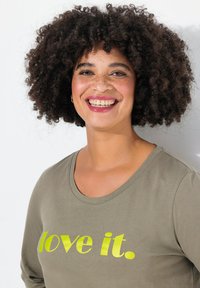 Olivi vihreä pitkähihaine paita, jossa on pyöreä kaula-aukko ja neonkeltainen teksti "love it." lihavoituna. Sujuva pinta, rento istuvuus.