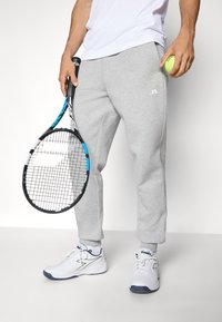 Gray sweatpants with a logo on the left, white athletic shoes, holding a tennis racket and a tennis ball. Simple, casual athletic wear.
