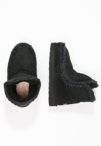 Stivali alla caviglia in suede nero con una morbida fodera pelosa e dettagli intrecciati lungo i bordi. Suola in gomma per aderenza e durata.