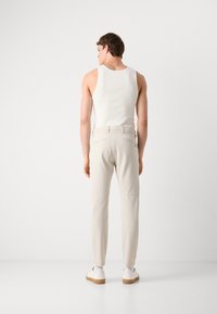 Calças bege claras com bolsos traseiros e costuras, combinadas com uma t-shirt justa branca. Modelo é mostrado de costas contra um fundo simples.