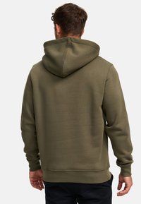 Sudadera color verde oliva con bolsillo tipo canguro, que cuenta con capucha ajustable, textura suave y puños acanalados, con costuras visibles en las uniones.