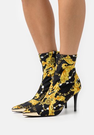 Zwarte stoffen enkellaarsjes met een gouden barok patroon, spitse neus en een met goudaccenten versierde hak. Voorzien van een ritssluiting aan de achterkant.