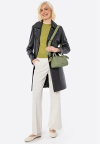 Cappotto trench in pelle nera, top verde, pantaloni a palazzo crema e ballerine beige. Piccola borsa verde con dettagli dorati.