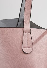Roze leren tote bag met een gestructureerd oppervlak, voorzien van zwarte randen, twee hengsels en zichtbare stiksels. De binnenkant heeft een grijze voering.