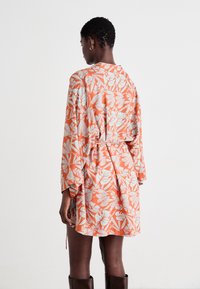 Robe à motifs floraux orange avec des manches longues, taille cintrée et coupe décontractée. Présente des motifs de feuilles bleu clair et une texture de tissu douce.