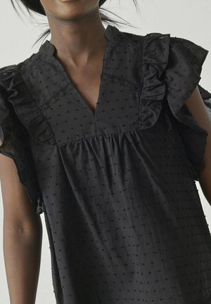 Sort bluse med v-hals, delikate ruffles på ærmerne og teksturerede prikker. Stoffet ser let og med en subtil glans.