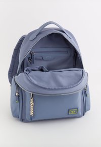 Mochila de tela azul con múltiples compartimentos con cremallera, tapa redonda y un bolsillo texturizado como acento. Interior forrado con secciones organizativas.