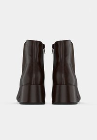 Brūni ādas potīšu zābaki ar elegantu dizainu, kas izceļas ar nedaudz izliektu papēdi un sānu rāvējslēdzējiem ērtākai uzvilkšanai. Gluda, mirdzoša tekstūra.