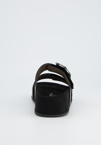 Sandal nero con tomaia morbida e strutturata, open back, due cinghie e suola spessa. Include un accento metallico per la chiusura.
