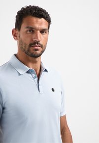 Lichtblauw polo shirt van katoen, met een klassieke kraag, drie knopen en een klein merklogo op de linkerkant van de borst.