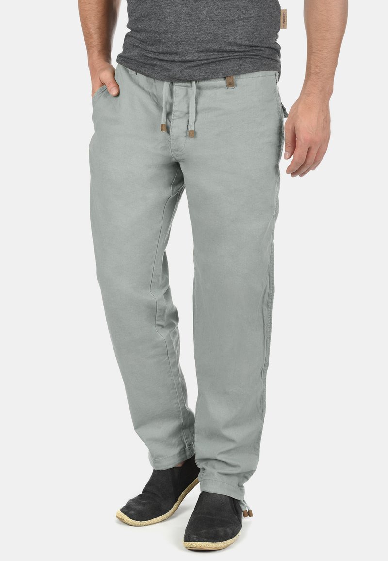 Pantalones de algodón gris claro con un corte relajado, cintura con cordón, bolsillos laterales y una textura sutil. Combinados con zapatos negros.