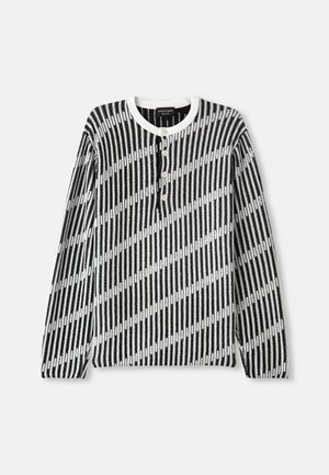 Pull à manches longues noir et blanc avec un motif de rayures diagonales, doté d'un col rond et de quatre boutons sur le devant. Tissu texturé.