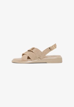 Sandalia beige de ante con punta abierta, tiras cruzadas, hebilla ajustable en el tobillo y suela baja y plana.