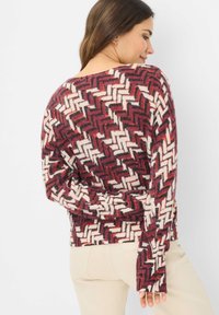 Maglione a maglia con motivo a zig zag nei colori rosso, crema e nero, maniche lunghe e scollatura rotonda. Texture morbida e vestibilità comoda.