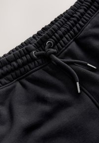 Zwarte sportbroek met een brede elastische tailleband met geplooide textuur, een trekkoord met metalen uiteinden en een gladde stof.