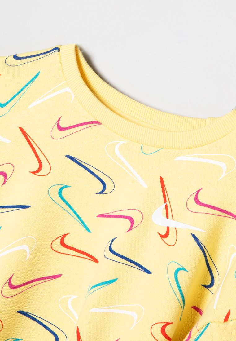Sudadera de algodón amarilla con un patrón de logotipos de swoosh de Nike en multicolor (rosa, azul, rojo y verde) por toda la prenda. Cuello acanalado.