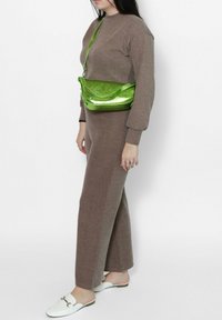 Completo a maglia marrone in due pezzi con maniche lunghe e pantaloni a gamba larga, abbinato a una borsa a tracolla verde brillante e a scarpe bianche slip-on.