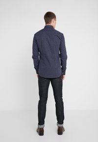 Camicetta blu marina con piccoli pois bianchi, maniche lunghe, vestibilità aderente, abbinata a jeans scuri e scarpe marroni.