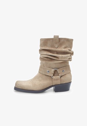 Beige Wildleder-Stiefelette mit rutschigem Schaft, breitem Riemen mit silbernem Beschlag und kreisförmigem Detail sowie einem niedrigen Blockabsatz.