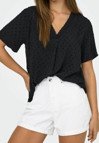 Black textured blouse with a v-neck and short sleeves, featuring a dotted pattern, paired with white denim shorts.