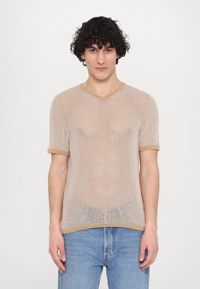 Haut en tricot beige clair à manches courtes avec un design en maille. Il présente un décolleté en V et une bordure contrastante en beige plus foncé le long de l'encolure et des manches.