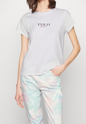 Szara bawełniana koszulka z krótkim rękawem i okrągłym dekoltem, z logo "POLO" w ciemnoniebieskim kolorze z czerwonym akcentem. Nosi się z pastelowymi jeansami w stylu tie-dye.