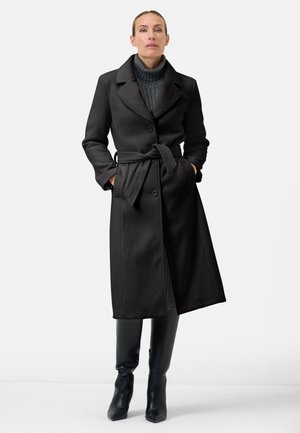 Black wool blend coat with a belted waist, large collar, and button closure. Worn over a ribbed turtleneck and paired with knee-high boots.