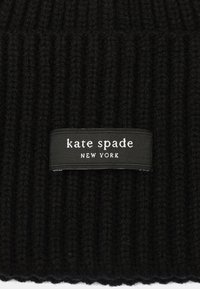 Tejido de punto acanalado negro con una etiqueta que dice "kate spade NEW YORK" en texto blanco sobre un fondo rectangular negro.