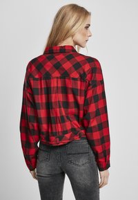 Rød og svart rutete flanellskjorte med krage, lange ermer og mansjetter; har en knappet bakstykke og en cropped design.