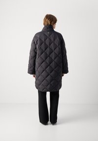 Zwarte gewatteerde pufferjas met een hoge kraag, voorzien van een ruitpatroon en een losse pasvorm. Gecombineerd met zwarte gestructureerde broek en hakken.
