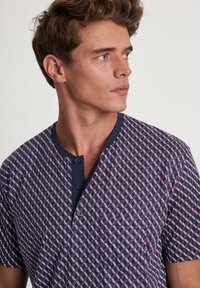 Short-sleeve shirt made of patterned fabric in navy with a geometric design in red and white; features a button placket and a chest pocket.