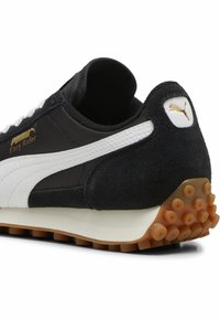 Mustvalge Puma Easy Rider tennis, millel on suede ja tekstiilist pealis, kuldne logo ja kummist tallad, millel on ringikujulised haardelad.