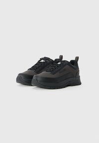 Une paire de baskets basses noires et gris foncé avec des semelles épaisses, un système de laçage, des languettes de tirage et un marquage sur les côtés et la languette.