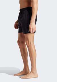 Black swim shorts with an elastic waistband, featuring a small white logo on the left side. The fabric appears smooth and lightweight.