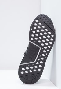 Schwarze Sneakersohle mit einer strukturierten GummOberfläche. Verfügt über hexagonale und kreisförmige Muster sowie einen weißen Streifen an der Ferse.