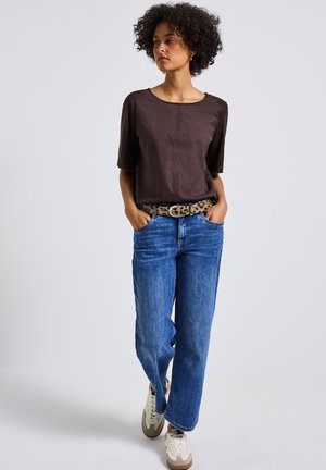 Braunes Wildleder-Top mit kurzen Ärmeln, blaue weite Jeans, Gürtel mit Leopardenmuster und weiße Sneaker mit braunen Akzenten. Einfaches, lässiges Outfit.