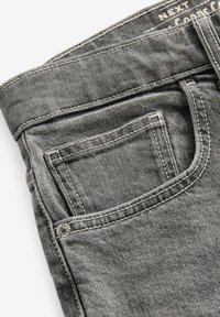 Graue Denim-Jeans mit einem mittelhohen Bund, ausgestattet mit Kontrastnähten und einer kleinen Vordertasche. Glatte Textur und klassischer Schnitt.