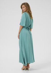 Teal, long maxi dress with short sleeves, gathered waist tie, and side slits. Smooth texture, flowing design, minimalist style.