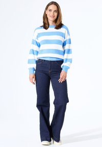 Blauw-wit gestreepte gebreide trui met een ronde hals en ribbelstructuur, gecombineerd met donkerblauwe wijde jeans en lichte schoenen.