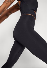 Black high-waisted leggings made from stretchy fabric, featuring a smooth texture and flat seams for comfort and performance.