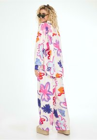 Top exagéré coloré et pantalon large avec un motif floral en rose, violet, orange et bleu sur un fond clair.