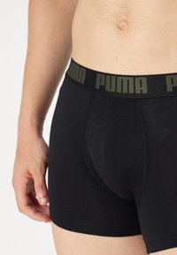 Fekete boxer alsónadrág, pamutból készült, sima textúrával, széles derékkal, amelyen oliva zöld "PUMA" felirat található.