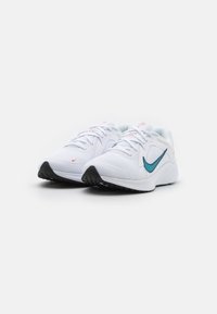 Zapatillas deportivas blancas con una parte superior de malla texturizada, logo en forma de swoosh color turquesa, acentos rosas en la lengüeta y un patrón de suela de goma negra.