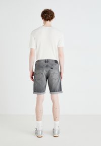 Sive jeans kratke hlače s zavihanimi robovi, zadnjimi žepi in črno oznako. Nošene z belo rebrasto majico in srebrnimi športnimi copati.