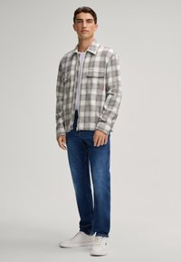 Giacca a quadri in grigio, bianco e sottili tonalità di blu, dotata di due tasche sul petto, abbinata a jeans blu e sneakers bianche.