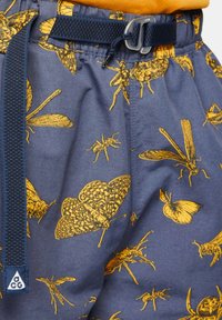 Marina shorts med ett mönster av gula insekter och fjärilar, elastisk midja med ett justerbart marina bälte, samt en liten logotyp nära midjan.