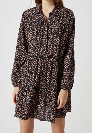 Robe noire à manches longues avec un imprimé floral en rose et vert. Dotée d'un col à boutons et d'un ourlet en volants à niveaux. Tissu léger et fluide.