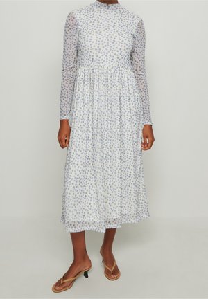 Robe à manches longues avec un col montant, fabriquée en tissu léger à base blanche et motif floral bleu. Design fluide, de longueur mi-longue avec taille froncée.