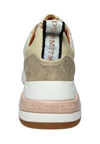 Sneaker beige e oro con una finitura testurizzata, dotata di una suola intermedia bianca e di un grande gancio posteriore con accenti neri e argentati.
