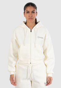 Opzijrits hoodie in off-white, met een losse pasvorm en voorzakken. Beschikt over een capuchon met trekkoord en geborduurde tekst op de borst.